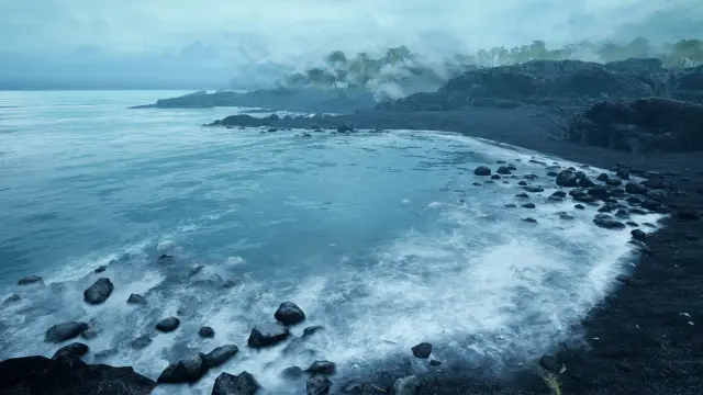 Waves breaking on a black pebble beach below a foggy headland